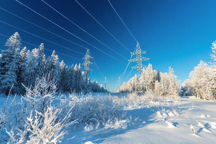 Electrical wires of overhead power line or electrical transmission line covered by snow in the winter forest adhering to IEC 60652:2021.