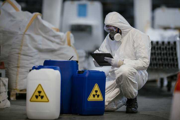 Protected worker measuring low-level radioactive waste adhering to ANSI/ANS-16.1-2019 (R2024).
