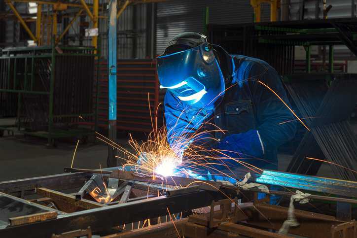Industrial Welder holding welding Torch with welding sparks with equipment adhering to ISO 17846:2004.