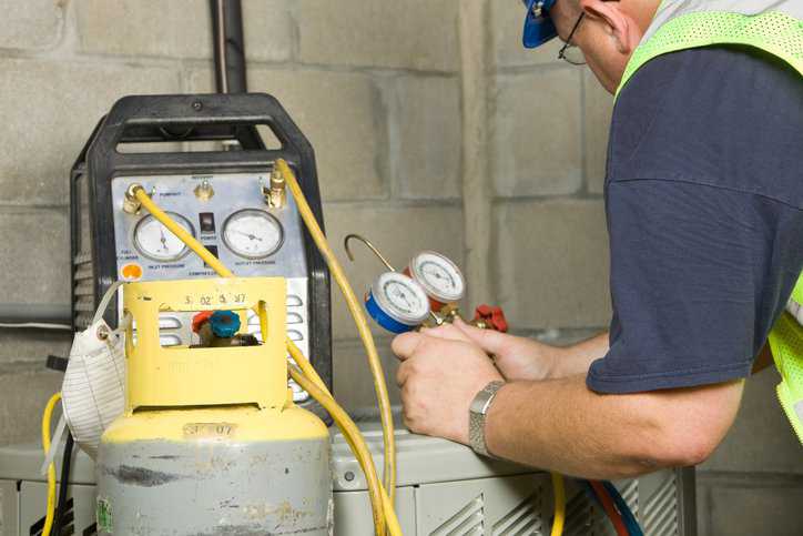 A service technician is using gauges a recovery pump and tank to remove refrigerant from a residential air conditioning system adhering to IEC 60335-2-104:2021.