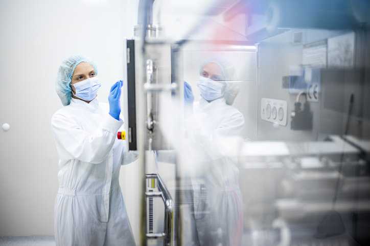 Lab expert in cleansuit conducting an internal audit by looking at fume hood.