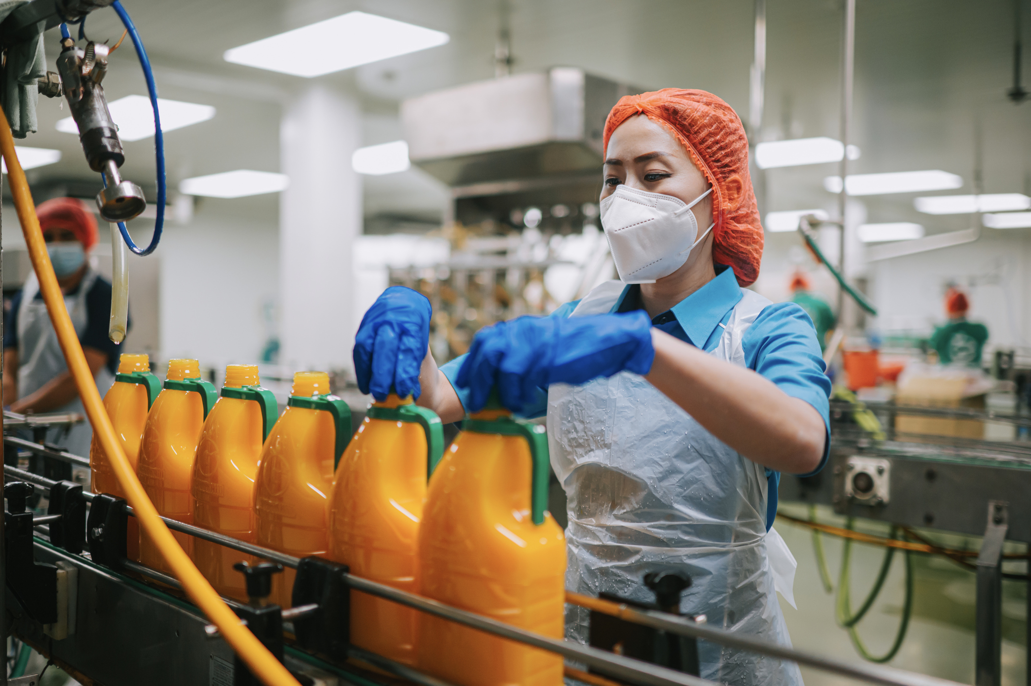 Worker tightening bottle caps in orange juice assembly line with ISO 22000 processes.