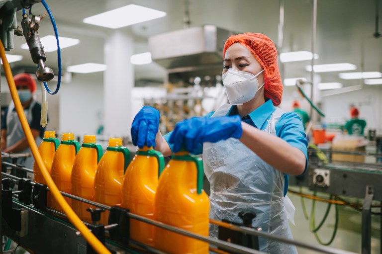 Worker tightening bottle caps in orange juice assembly line with ISO 22000 processes.