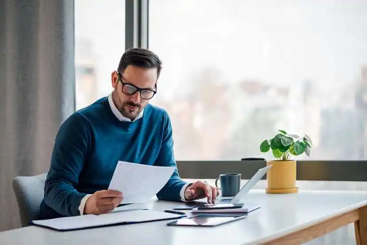 Man in open office uploading tax exempt certificate to the ANSI Webstore via computer and looking at paper.