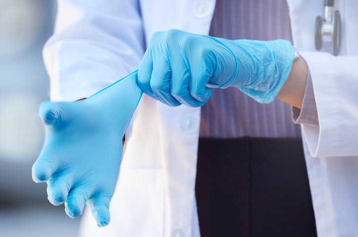 Doctor putting on polyvinyl chloride (PVC) medical examination gloves that adhere to ISO 11193-2:2006.