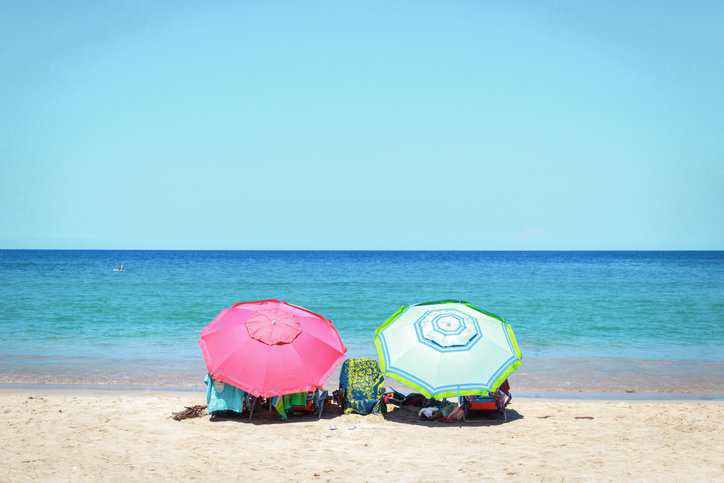 Two colorful beach umbrellas set on a sandy, sunny beach that adhere to ASTM F3512-21.