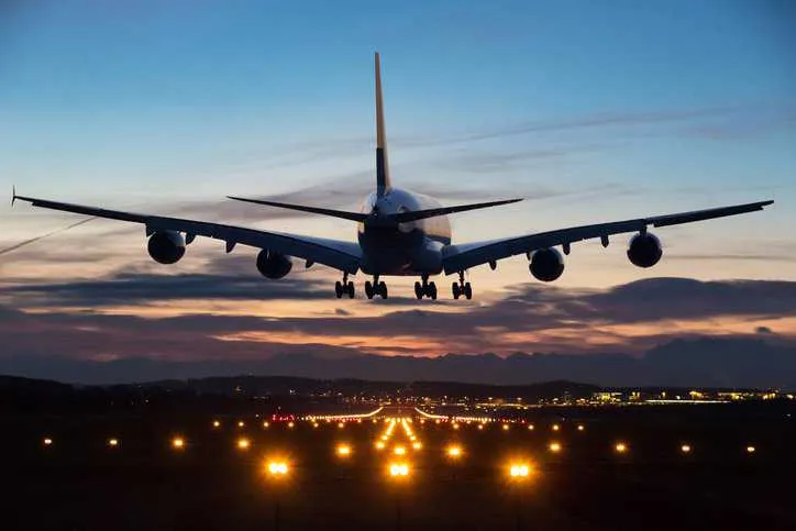 An airplane just before landing in the early morning with runway lights in the foreground that adhere to ANSI/IES RP-37-22 airport lighting requirements.