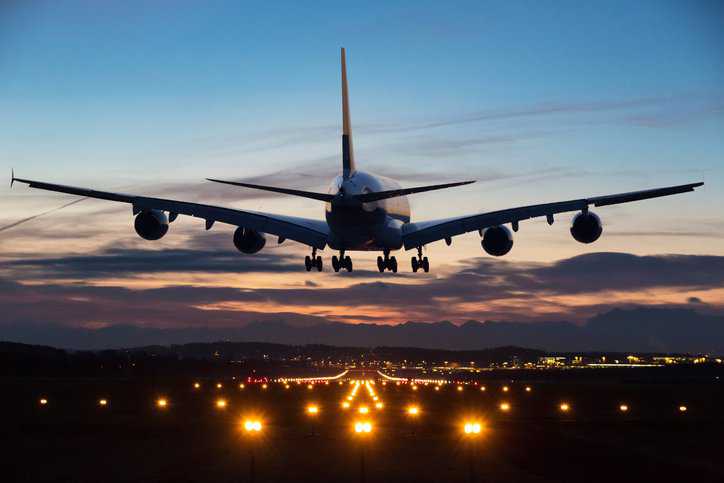 An airplane just before landing in the early morning with runway lights in the foreground that adhere to ANSI/IES RP-37-22 airport lighting requirements.