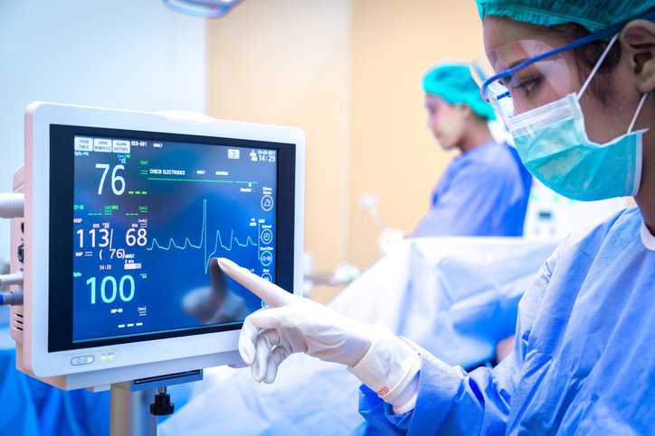 Female surgeon using monitor in operating room that adheres to health information technology and risk management in AAMI 80001-GS:2011 and IEC 80001-1:2021.