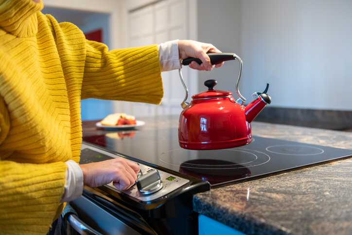 Woman placing red kettle on stovetop to heat.
