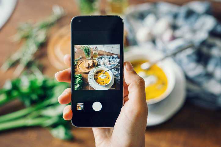 Woman taking photo of pumpkin soup with smartphone that has a camera that adheres to IEEE 1858-2023.