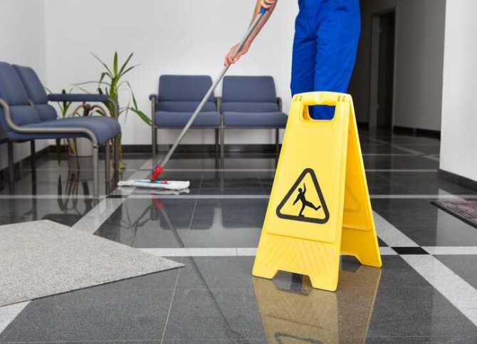 Worker mopping floor near slip caution sign.