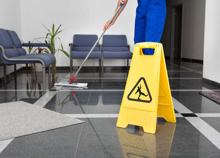 Worker mopping floor near slip caution sign.