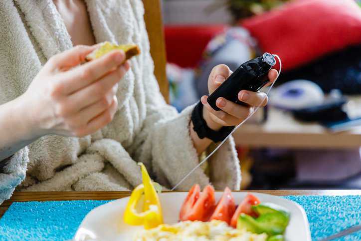 Modern diabetes treatment, woman checking glucose level and dosing insulin with insulin pump before her healthy breakfast.