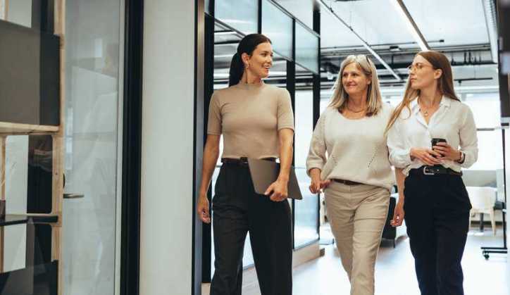 Three successful female entrepreneurs walking together in an office led by women, adhering to IWA 34:2021.