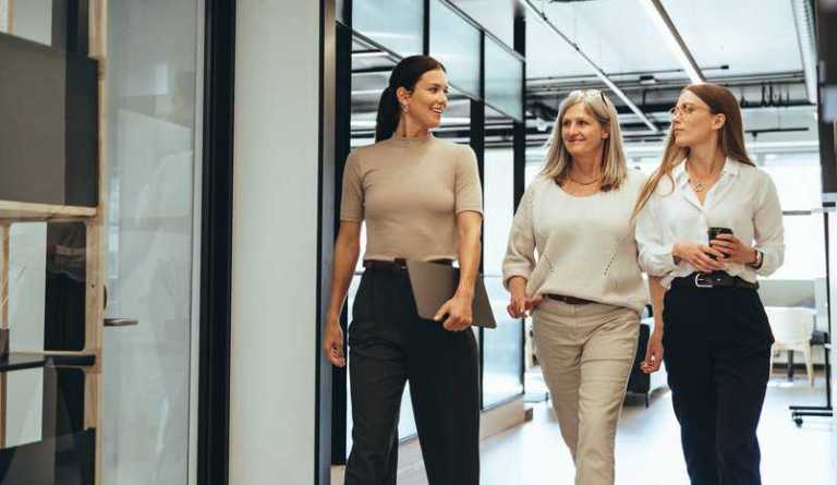 Three successful female entrepreneurs walking together in an office led by women, adhering to IWA 34:2021.