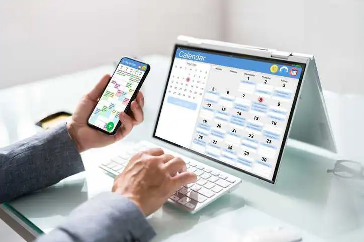 Appointment schedule planner and date calendar on hybrid laptop, adhering to ISO 21802:2019 assistive product requirements, helping an individual with cognitive limitations manage her time.