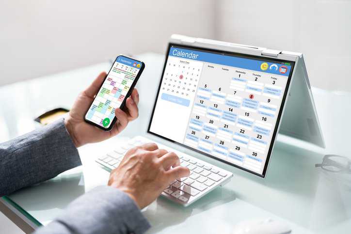 Appointment schedule planner and date calendar on hybrid laptop, adhering to ISO 21802:2019 assistive product requirements, helping an individual with cognitive limitations manage her time.