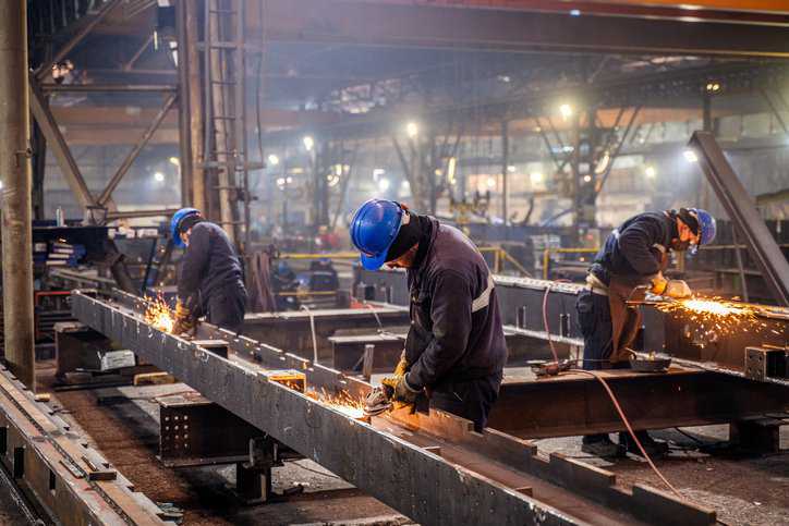 Metal workers using a grinder that adheres to ANSI/ASSP Z9.6-2018.