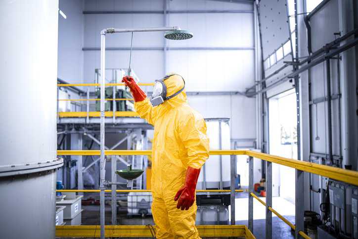 Worker in chemicals production plant taking a shower after accident washing away the corrosive acid with an emergency shower adhering to OSHA 1910.151(c).