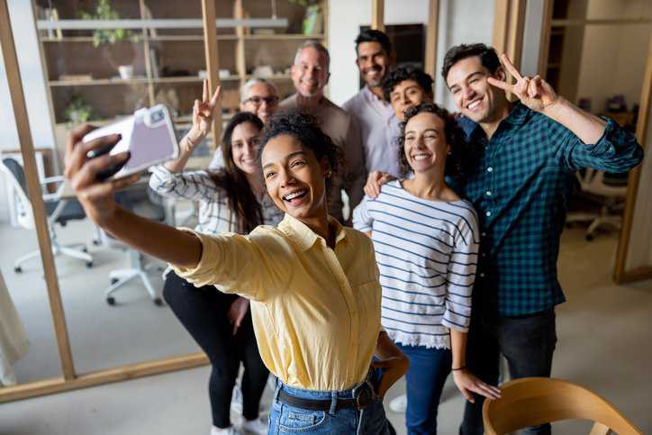 Happy business team taking a selfie at the office using a cell phone for social media purposes that adhere to ARMA TR 21-2012 guidelines.