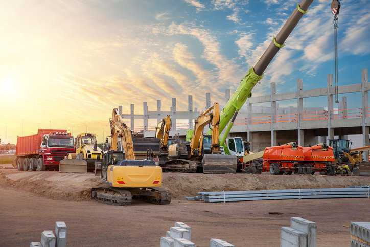 Many different colorful heavy industrial earth-moving machinery at construction site parking that adhere to ISO 15143-1:2010.