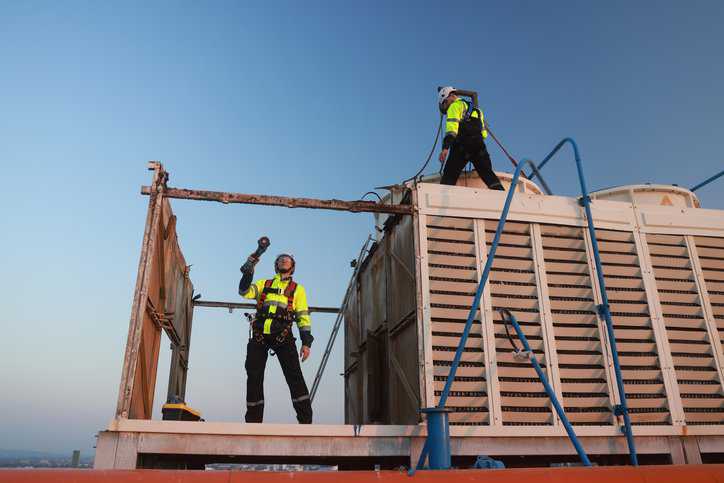 Two technicians doing construction work at an unprotected edge and adhering to safety requirements in ANSI/ASSP A10.18:2023.
