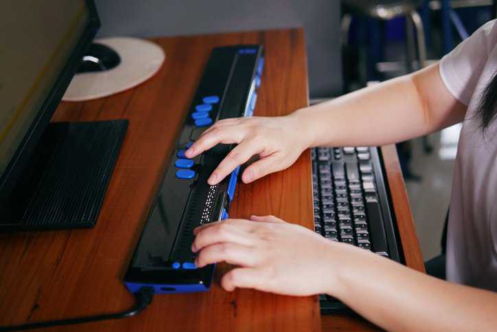 Person with cognitive disability's hands using computer braille terminal technology assistive device that adheres to ANSI/RESNA CA-1:2018..