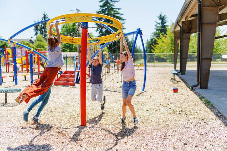 A group of tween girls and boys have fun playing together on a playground that adheres to ISO/TR 24666:2023 safety specifications.