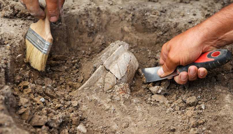 Archaeological Dig Closeup of brush and hands excavating at archaeological site.