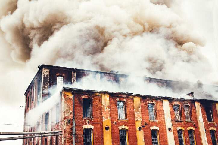 Smoke rising above old brick factory fire that didn't follow the 2024 International Fire Code (ICC IFC-2024).