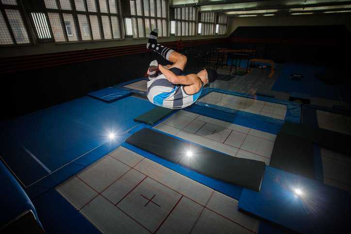 Gymnast doing a summersault from a trampoline court, practicing trampolining for the Olympics, that adheres to ASTM F2970-22.