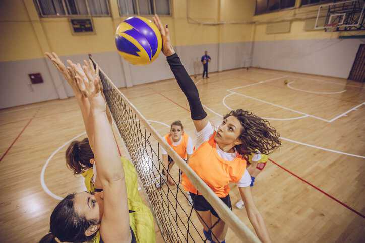 Children in their school gymnasium playing volleyball with equipment adhering to ASTM F3683-24.