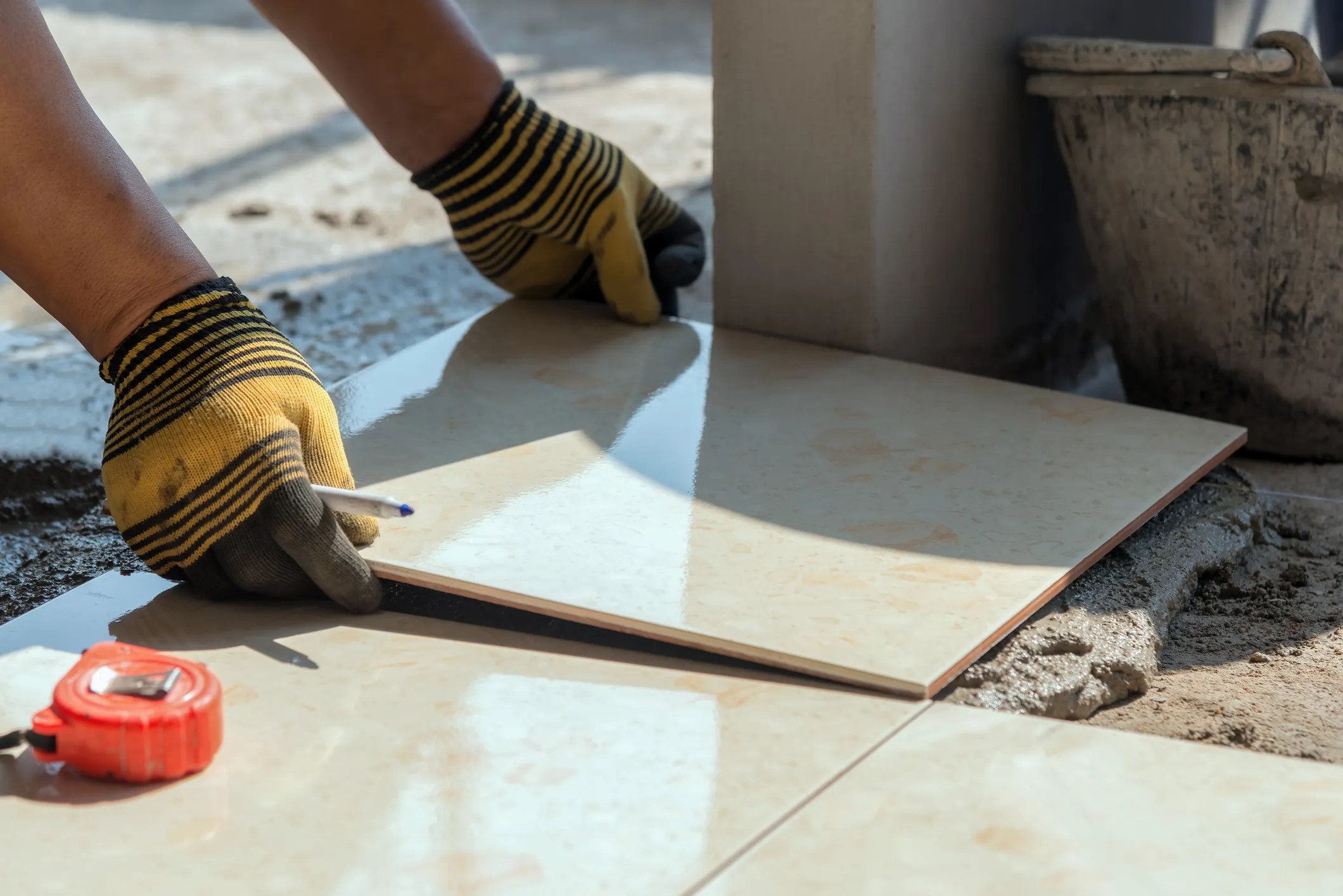 Setting ceramic tile onto grout while wearing yellow striped gloves