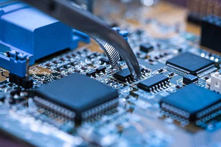 Blue circuit board being checked with tweezers via IPC A-610J-2024 defect and problem testing.