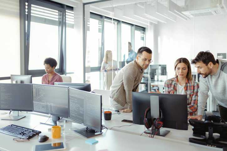 Young AI programmers and IT software developers team programming on desktop computer in startup company share office space to assure that the serial-attached SCSI (SAS) Protocol adheres to INCITS 554-2023.