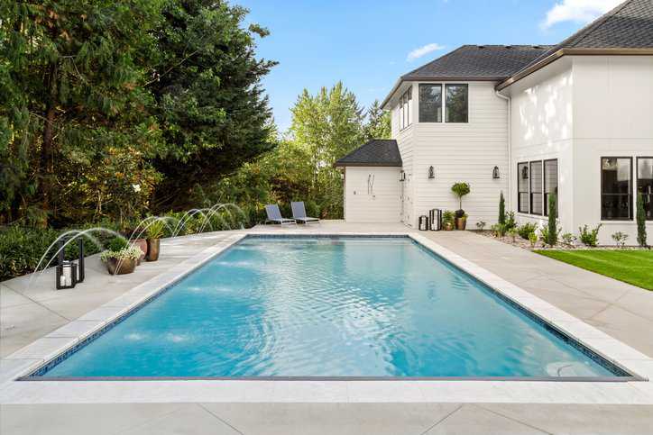 Beautiful swimming pool in a backyard on a sunny day equipped with a safety vacuum release system (SVRS) that adheres to ASME A112.19.17-2010 (R2023).