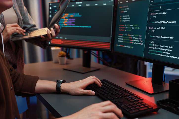 IT developers discussing intelligent website development coder system running data online two screens with laptop for secure data transfer that adheres to INCITS 542-2022.