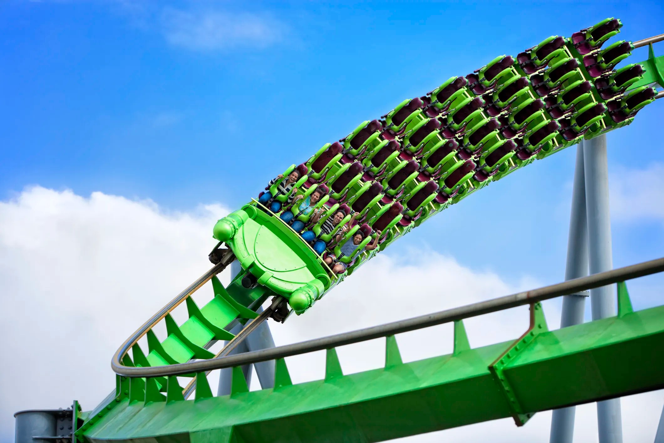 Green roller coaster on loop with passengers enjoying ASTM F2291-25 amusement thrills.