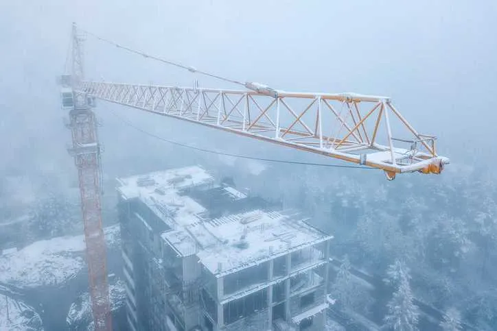 Yellow construction crane above frozen cityscape building and trees in winter.