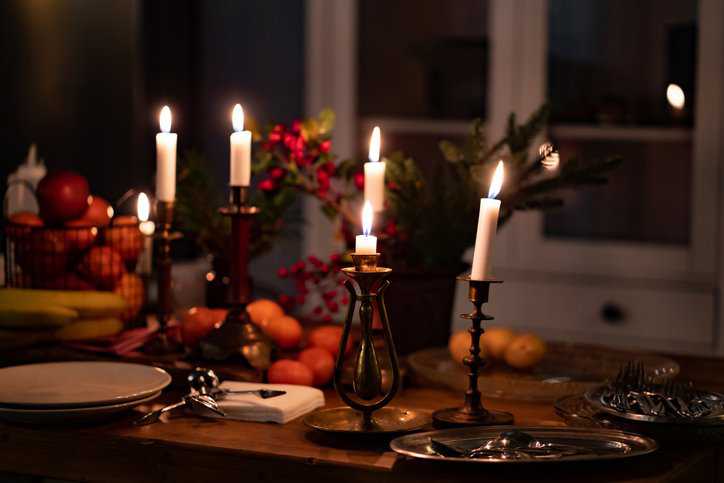 Candle accessories, such as candle holders and candle burners, on a wooden table decorated for Thanksgiving dinner that adhere to candle fire safety specifications in ASTM F2601-18.