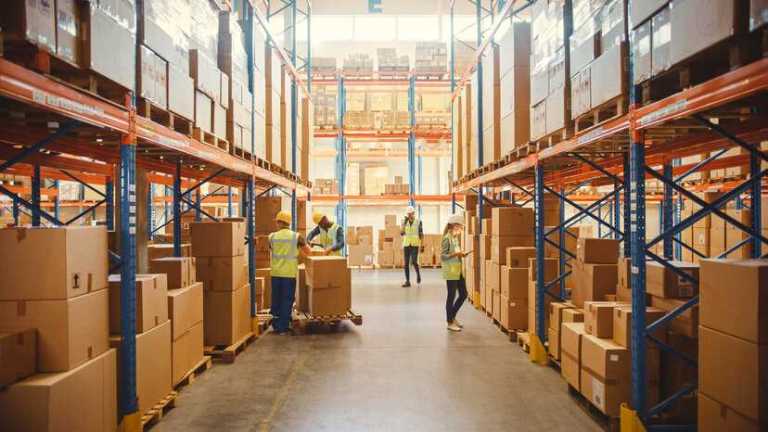 Retail warehouse with workers in hallway surrounded by cardboard boxes on racks adhering to conformity assessment processes.