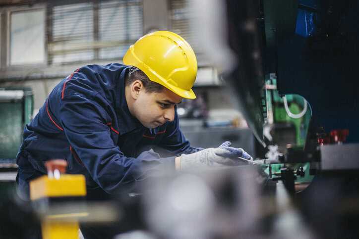 Worker in hard had conducting preventative maintenance of metal sheet press machinery.