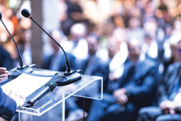 Public speaker at business conference using a loudspeaker and microphone that passed ANSI/ASA S3.2-2020 speech intelligibility testing.
