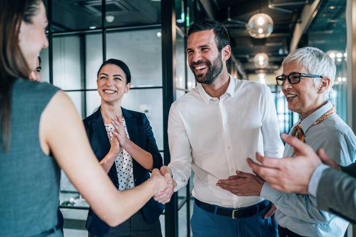 Cheerful Business people shaking hands in the office after learning how much money they saved by implementing accreditation services for their organization.