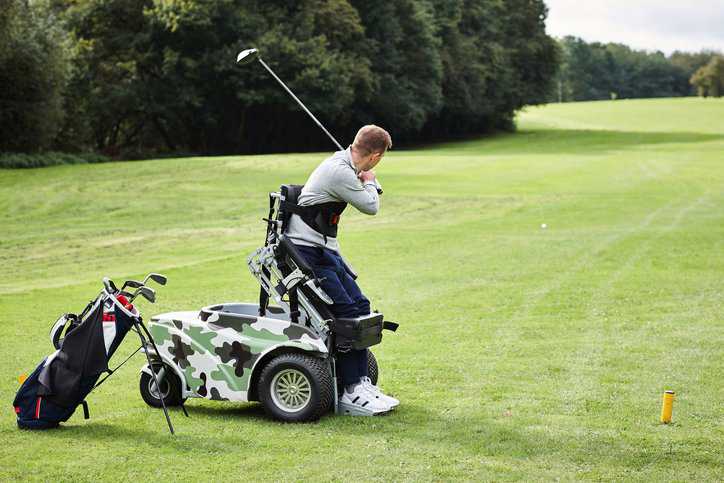 Man with an impairment using an adaptive golf cart that adheres to ANSI/RESNA ASE-2:2012 (R2018), while he enjoys golfing on a green golf course.