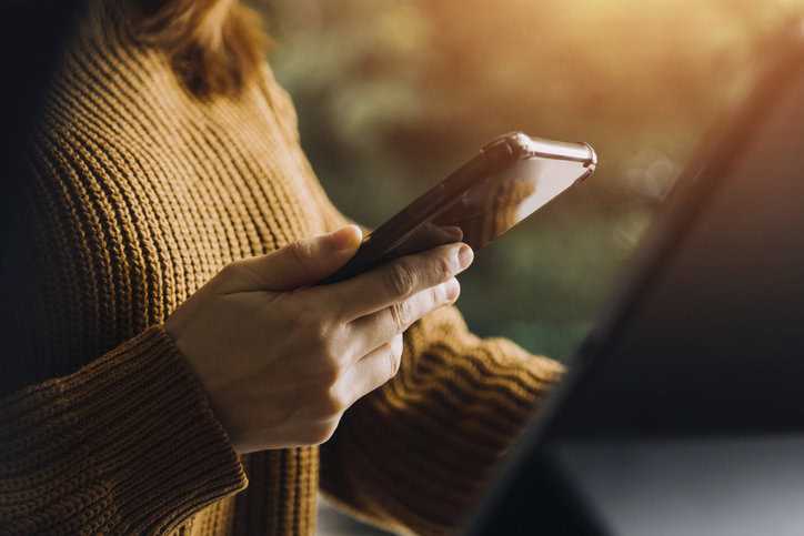 Woman on phone in brown sweater contacting ANSI