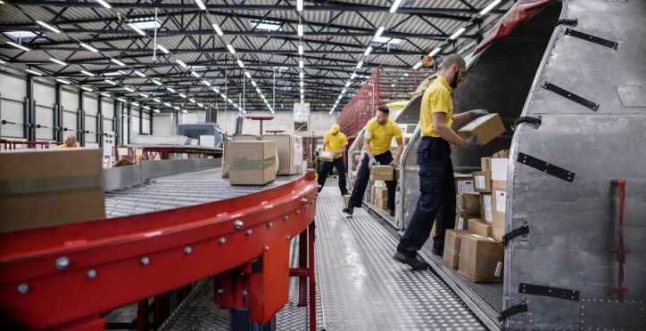 Workers loading boxes onto red ergonomic conveyor.
