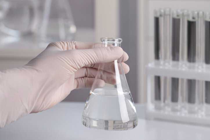 Scientist holding conical flask with reagent water, adhering to ASTM D1193-24, in a clinical laboratory.