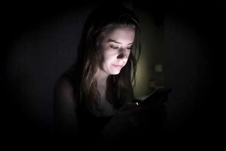 Woman looking at phone blue light at night, not able to sleep.